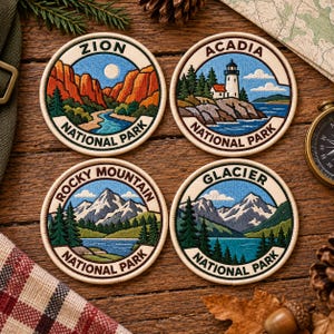 May include: Four circular embroidered patches featuring national park landscapes. The Zion patch shows red rock canyons and a river. The Acadia patch depicts a lighthouse on a rocky coast. The Rocky Mountain and Glacier patches show snow-capped mountains, pine forests, and lakes.