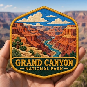May include: A hexagonal embroidered patch featuring a landscape of the Grand Canyon with red rock formations, a winding blue river, and green trees under a blue sky with white clouds. The bottom section is dark green with the text GRAND CANYON NATIONAL PARK.