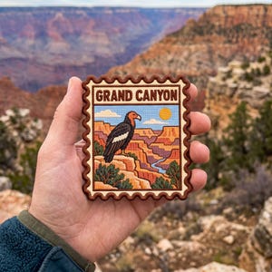 May include: A rectangular embroidered patch with a scalloped edge featuring a California condor perched on a rock formation overlooking the Grand Canyon. The text GRAND CANYON is printed in brown at the top of the patch against a light background.