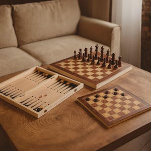 Könnte beinhalten: Ein hölzernes Backgammon-Spielbrett mit schwarzen und hellen Holzspitzen, ein Schachbrett aus Holz mit dunkelbraunen und hellen Figuren sowie ein Damebrett aus Holz mit dunkelbraunen runden Spielsteinen auf einem Holztisch.