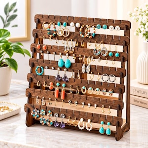 May include: A dark brown wooden jewelry organizer stand with multiple horizontal slats featuring notched edges for hanging various earrings, including turquoise, coral, and beaded styles, arranged in rows on a flat surface.