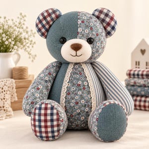Pu&ograve; includere: Un orsacchiotto patchwork realizzato con vari motivi in tessuto, tra cui blu tinta unita, stampa floreale, strisce blu e bianche e un motivo a quadri rosso, bianco e blu. L'orso presenta occhi a bottone neri, un naso ricamato e finiture in pizzo.