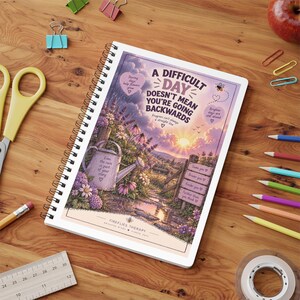 May include: A spiral-bound notebook featuring a sunset landscape illustration with a watering can, flowers, and the text: A DIFFICULT DAY DOESN'T MEAN YOU'RE GOING BACKWARDS. Additional text includes: Even the rain is part of your story, Some you, Braver you, Kinder you, Further than you think, and Fireflies Therapy.