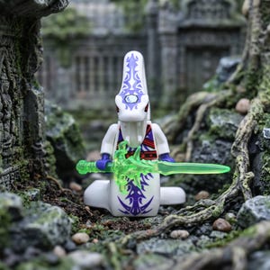 May include: A white plastic snake-like minifigure with purple tribal patterns on its head and body. The figure features red eyes, purple arms, and holds a translucent neon green sword. It has a long, coiled tail base instead of legs.