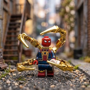 Puede incluir: Una minifigura de Spider-Man con un traje rojo y azul con detalles dorados, equipada con cuatro brazos mecánicos articulados de color dorado metálico que salen de la espalda. La figura tiene una máscara roja con ojos blancos sobre grava oscura.
