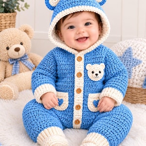 May include: A blue crocheted baby jumpsuit featuring a hood with bear ears, cream-colored trim, five brown buttons down the front, two pockets with small blue heart accents, and a small bear face applique on the chest with cream-colored cuffs.