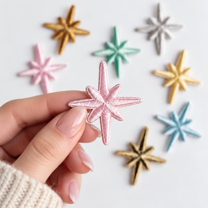 May include: A collection of eight embroidered star-shaped patches in various colors including pink, gold, silver, teal, and light blue. Each patch features a multi-pointed star design with a stitched texture and a raised center point.