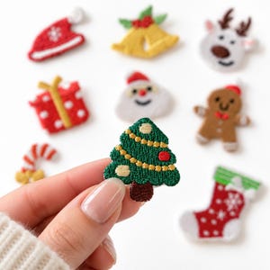 May include: A collection of small embroidered Christmas-themed patches including a red hat, yellow bells, a reindeer, a red gift, Santa Claus, a gingerbread person, a candy cane, a red stocking, and a green Christmas tree with gold garland.
