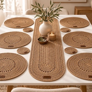 May include: A set of six round woven placemats, four small round coasters, and one long oval table runner, all crafted from tan fiber with a textured, concentric pattern and small brown leather-like rectangular labels attached to each piece.
