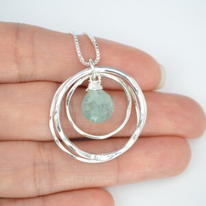 May include: A silver necklace with a pendant featuring two hammered circles and a light blue gemstone.