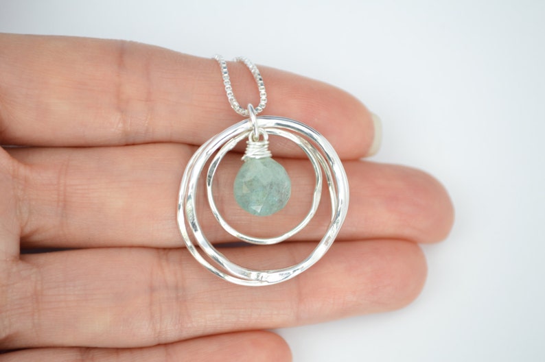 May include: A silver necklace with a pendant featuring two hammered circles and a light blue gemstone.
