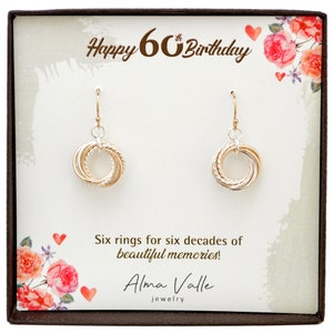 May include: A pair of gold and silver earrings with six rings, presented in a gift box with the text "Happy 60th Birthday" and "Six rings for six decades of beautiful memories!"  Alma Valle Jewellery.