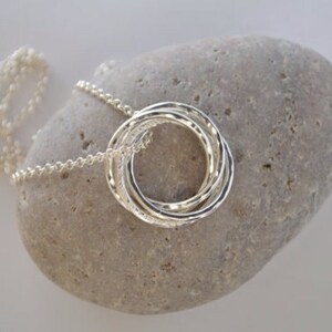 May include: A silver necklace with a pendant made of four interlocking rings. The pendant is textured and has a hammered finish.