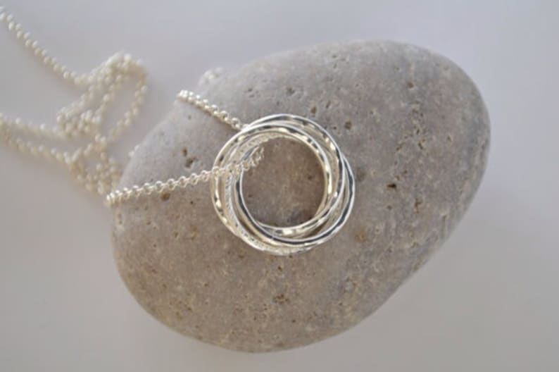 May include: A silver necklace with a pendant made of four interlocking rings. The pendant is textured and has a hammered finish.
