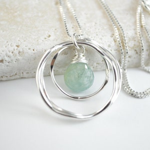 May include: A silver necklace with a delicate chain and a pendant featuring two intertwined circles with a light blue gemstone in the center.