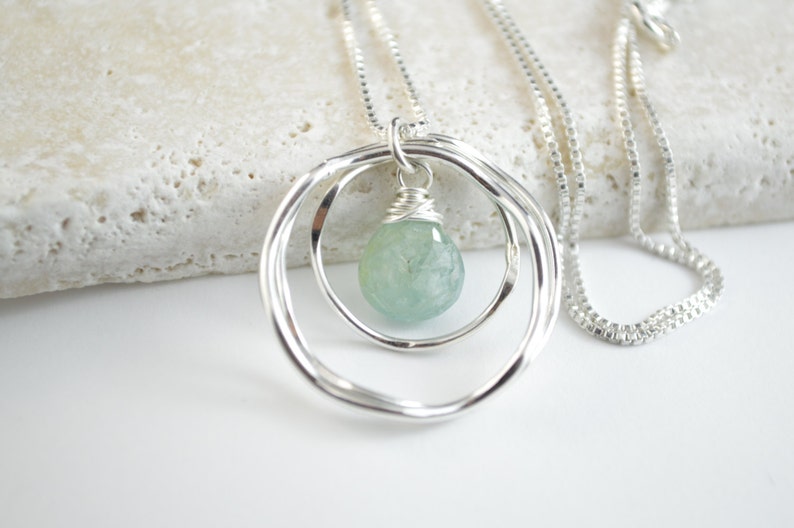 May include: A silver necklace with a delicate chain and a pendant featuring two intertwined circles with a light blue gemstone in the center.