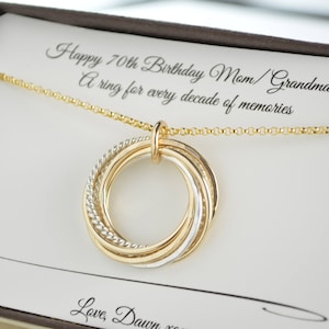 Peut inclure: Un collier en or avec un pendentif composé de sept anneaux entrelacés. Le pendentif est dans une boîte avec une carte qui dit "Joyeux 70e anniversaire Maman/Grand-mère ! Un anneau pour chaque décennie de souvenirs. Avec amour, Dawn."
