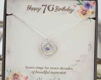 May include: A silver necklace with a pendant of seven intertwined rings and a blue gemstone. The necklace is displayed in a box with a white background and the text "Happy 70th Birthday" and "Seven rings for seven decades of beautiful memories!"
