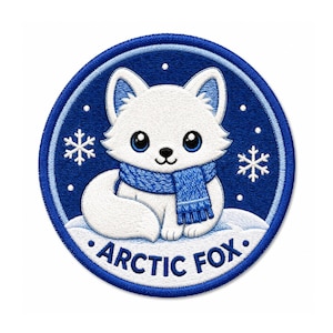May include: A circular embroidered patch featuring a white arctic fox with large black eyes wearing a blue knitted scarf. The fox sits on a snowy mound against a dark blue background with white snowflakes and the text ARCTIC FOX at the bottom.