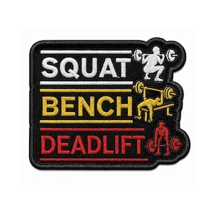 May include: A black embroidered patch featuring the text SQUAT in white, BENCH in yellow, and DEADLIFT in red. Each word is accompanied by a corresponding white, yellow, or red embroidered figure performing the respective weightlifting exercise.