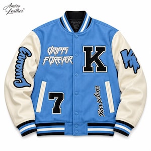May include: A light blue varsity jacket with cream-colored sleeves, featuring a black letter K, the number 7, and text reading Drips Forever and Knakctnon. The jacket has a snap-button front, striped ribbed cuffs, and a black collar.