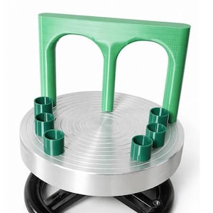 Puede incluir: Una herramienta para torno de alfarero con un disco metálico circular plateado con anillos concéntricos. Incluye un accesorio de plástico verde en forma de arco y seis pequeños soportes cilíndricos verdes sobre el disco.