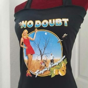 May include: A black tank top featuring a graphic print of the No Doubt Tragic Kingdom album cover. The design includes a person in a red dress standing in a field with a bare tree, yellow lemons, and the text No Doubt and Tragic Kingdom.