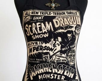 Puede incluir: Un top negro de estilo halter con un estampado de póster de película de terror vintage en crema y negro. El diseño incluye textos como Scream Dracula Show, Frankenstein Monster y Wolf Man. Se lleva un collar con colgante de murciélago bronce.