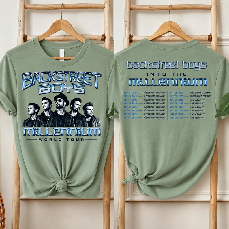 May include: A sage green t-shirt featuring a graphic of the Backstreet Boys with the text "BACKSTREET BOYS INTO THE MILLENNIUM WORLD TOUR" on the front and a list of tour dates and locations printed on the back in blue and white lettering.