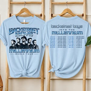 May include: A light blue t-shirt featuring a graphic of the Backstreet Boys on the front with the text Backstreet Boys Millennium World Tour. The back of the shirt displays the text Backstreet Boys Into The Millennium and a list of tour dates.
