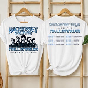 May include: A white t-shirt featuring a graphic of the Backstreet Boys with the text "BACKSTREET BOYS MILLENNIUM WORLD TOUR" on the front. The back displays the text "BACKSTREET BOYS INTO THE MILLENNIUM" and a list of tour dates in Germany and Nevada.