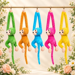 Pode incluir: Cinco macacos de pelúcia pendurados numa barra horizontal, cada um numa cor vibrante diferente: verde, laranja, azul, rosa e amarelo. Cada macaco apresenta um rosto de cor clara, olhos pretos e braços e pernas longos para pendurar.