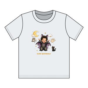 May include: A white short-sleeve t-shirt featuring a graphic of a baby dressed as a bat with purple wings, surrounded by a crescent moon, clouds, an owl, a ghost, and a black cat. The text "HAUNT RESPONSIBLY" is printed in yellow below the graphic.