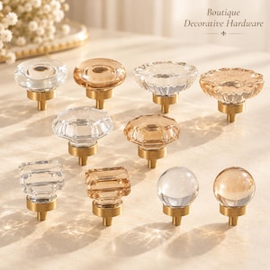 May include: A collection of ten cabinet knobs featuring clear and amber-toned glass tops with brass-colored metal bases. The shapes include round, faceted, and square designs. The text Boutique Decorative Hardware is visible at the top.