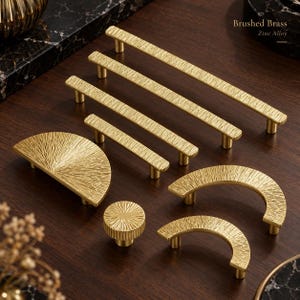 May include: A collection of brushed brass zinc alloy cabinet hardware including three linear bar pulls, two semi-circular pulls, one circular knob, and one half-circle pull, all featuring a textured, radiating line surface pattern.