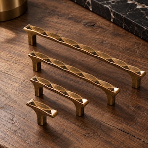 May include: A set of four brass-toned metal cabinet pulls and a knob, each featuring a textured, repeating diamond-shaped pattern along the top surface. The hardware pieces vary in length, ranging from a single knob to three elongated handles.