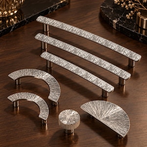May include: A collection of silver-toned cabinet hardware including three long straight pulls, two curved semi-circular pulls, one circular knob, and one fan-shaped pull. Each piece features a textured, rugged surface finish.