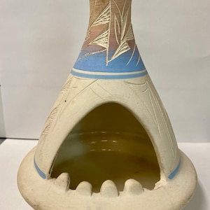 May include: A conical ceramic incense burner or ashtray with a wide base and a large arched opening. The exterior features a matte off-white finish with a blue band and etched geometric patterns near the top, which transitions to a tan color.