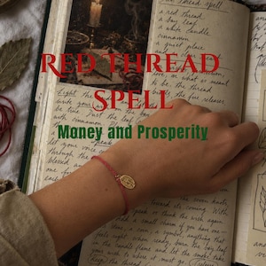 May include: A thin red string bracelet featuring a small gold-toned oval charm with an embossed figure. The bracelet is worn over an open book with handwritten text titled Red Thread Spell and Money and Prosperity, featuring a candle illustration.