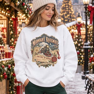 May include: A white crewneck sweatshirt featuring a vintage-style graphic of a steam locomotive train. The design includes the text The Midnight Railway, One Way To Wonder, and Boarding Every Christmas Eve, surrounded by festive holiday imagery.