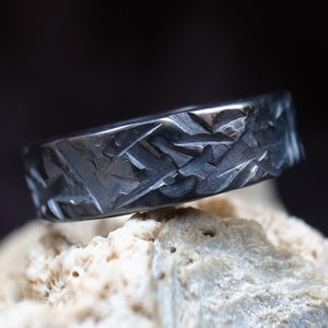 以下が含まれることがあります： 表面がテクスチャ加工された黒い金属製のリング。リングは隕石素材で作られており、ユニークで自然なパターンをしています。