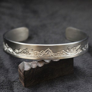 May include: A silver bracelet with a mountain range design engraved on the front.