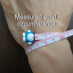 May include: A white measuring tape with red markings is wrapped around a person's wrist. The tape reads "20" inches. The text "Measured wrist circumference" is written above the wrist.