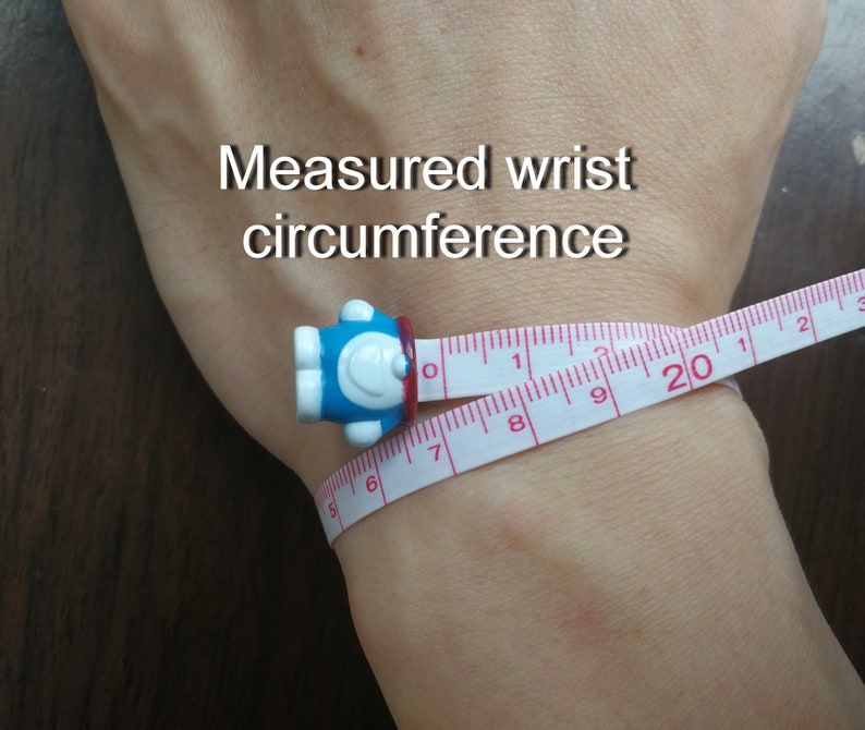 May include: A white measuring tape with red markings is wrapped around a person's wrist. The tape reads "20" inches. The text "Measured wrist circumference" is written above the wrist.