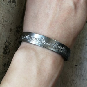 May include: A silver bracelet with a mountain range design engraved on the front.