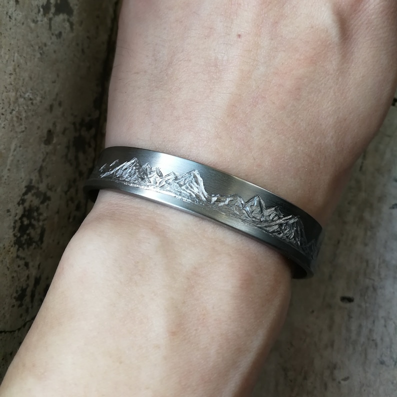 May include: A silver bracelet with a mountain range design engraved on the front.