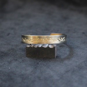 May include: A gold-toned metal bracelet with a mountain range design engraved on the front.
