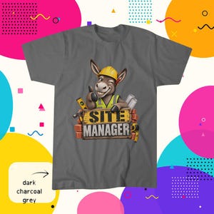 May include: A dark charcoal grey t-shirt featuring a cartoon donkey wearing a yellow hard hat and a high-visibility vest. The donkey is winking and giving a thumbs up behind a brick sign that reads SITE MANAGER, surrounded by construction tools.