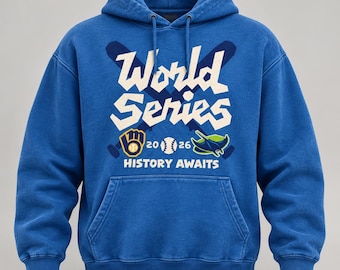 Puede incluir: Una sudadera con capucha azul que presenta un gráfico con dos bates de béisbol cruzados, una pelota de béisbol y el texto World Series 2026 History Awaits. El diseño incluye un logo amarillo y azul a la izquierda y una raya verde y azul a la derecha.