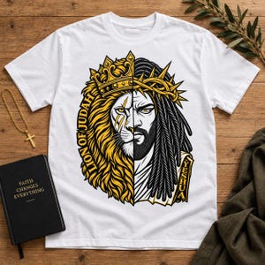 May include: A white t-shirt featuring a split-face graphic design. One side depicts a lion wearing a crown with the text LION OF JUDAH, while the other side shows a bearded figure wearing a crown of thorns with the text YESHUA printed vertically.